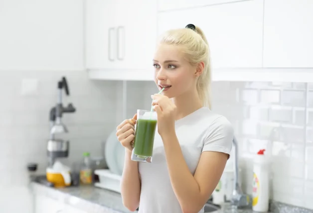 Joven mujer bebiendo jugo de batido verde en la cocina