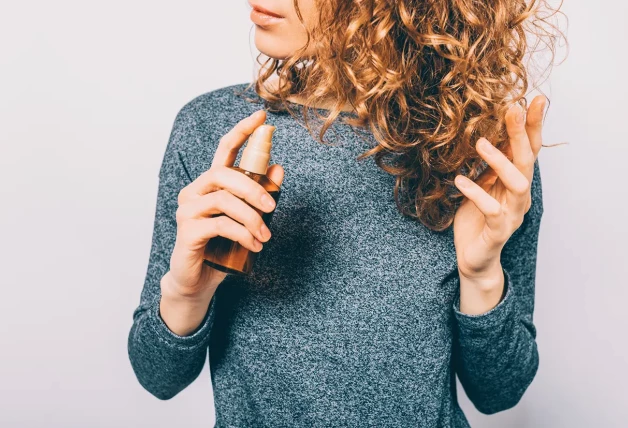 Chica con el pelo rizado aplicando serum a su cabello.