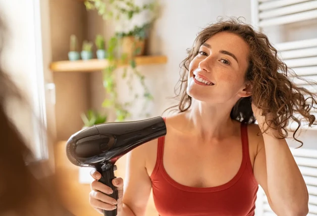 Chica sonriente con el pelo rizado usando un secador de pelo.