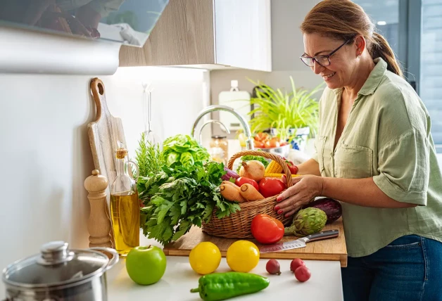 Señora en la cocina con un cesto lleno de vegetales.