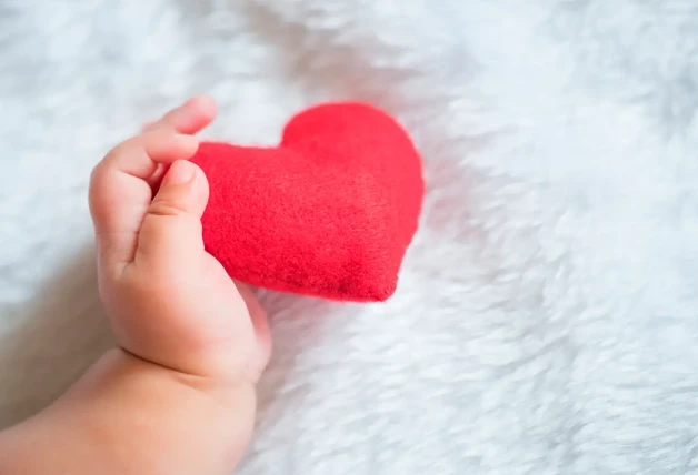 Mano de bebé cogiendo un corazón de peluche.