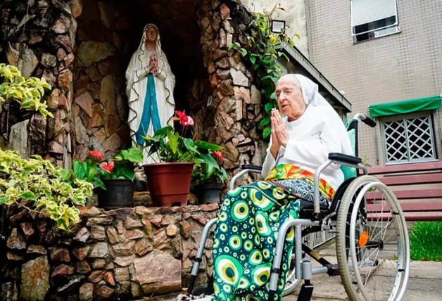 Monja el silla de ruedas rezandole a la virgen María.