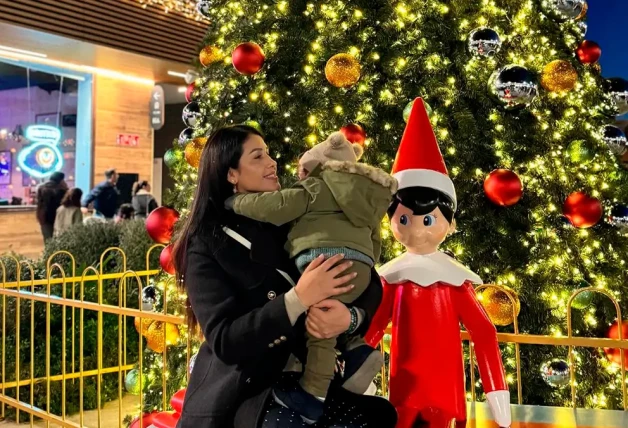 Gabriela Guillén con su bebé en brazos delante de un árbol de Navidad.