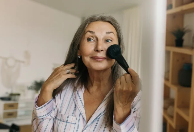 Mujer maquillándose la cara con una brocha ancha.