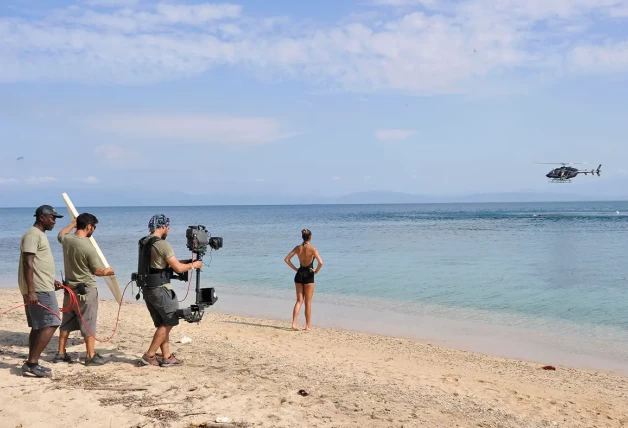 Cámara grabando desde una playa un escorzo de la presentadora de 'Supervivientes' observando a uno de los concursantes saltar desde un helicóptero