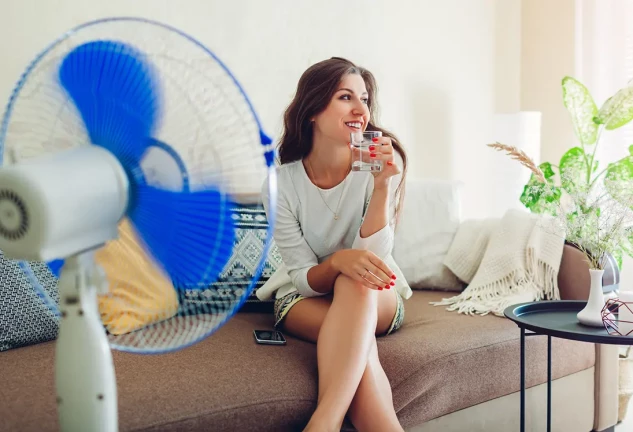 Chica bebiendo agua en el sofá de su casa delante del ventilador.