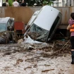 Un hombre y una mujer se abrazan junto a un montón de coches destrozados por la DANA.