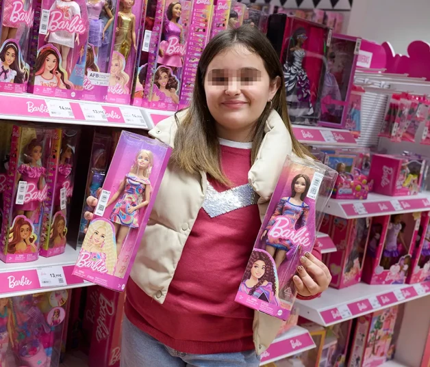 Niña posa con dos muñecas Barbie.