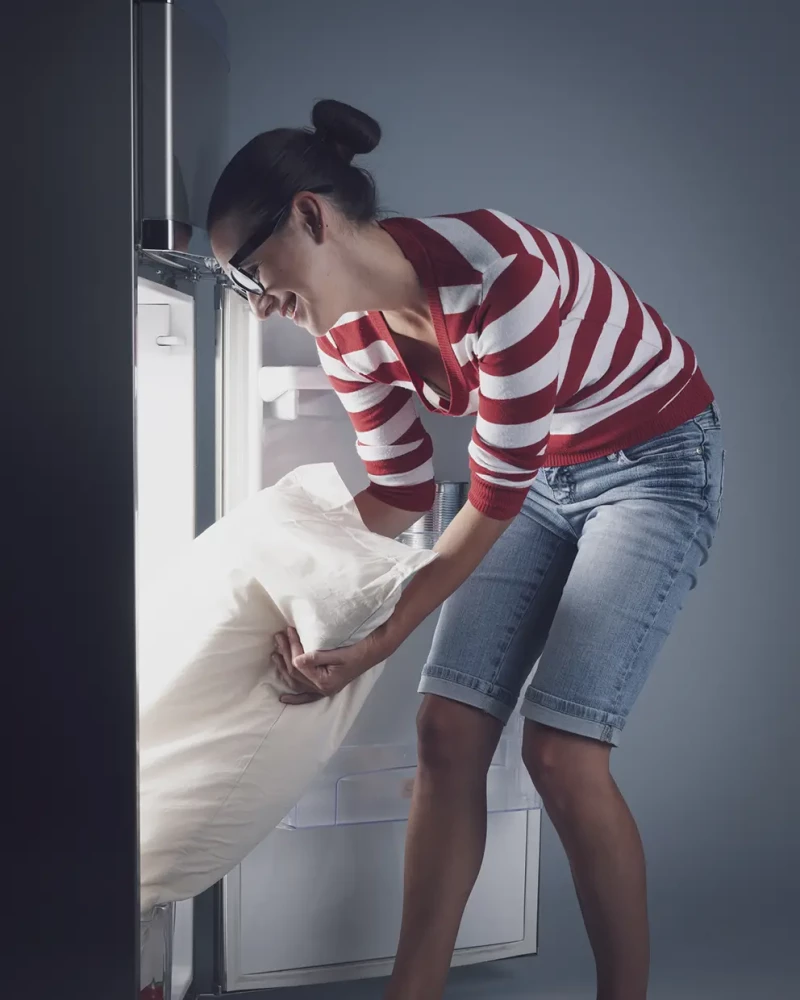 Mujer metiendo la ropa de cama dentro de la nevera para refrescarla.