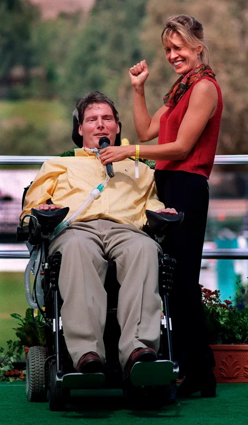 Christopher Reeve hablando al público y su mujer le sujeta el micrófono.