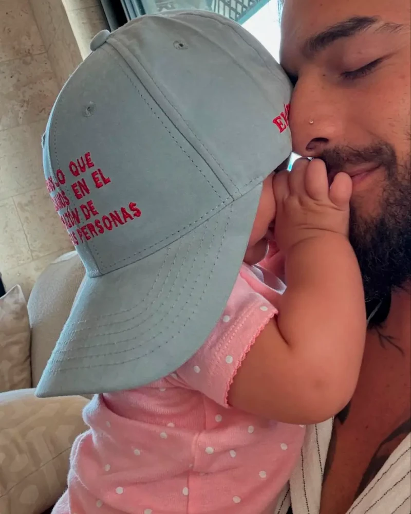 Maluma con su hija en brazos que lleva una de sus gorras en la cabeza