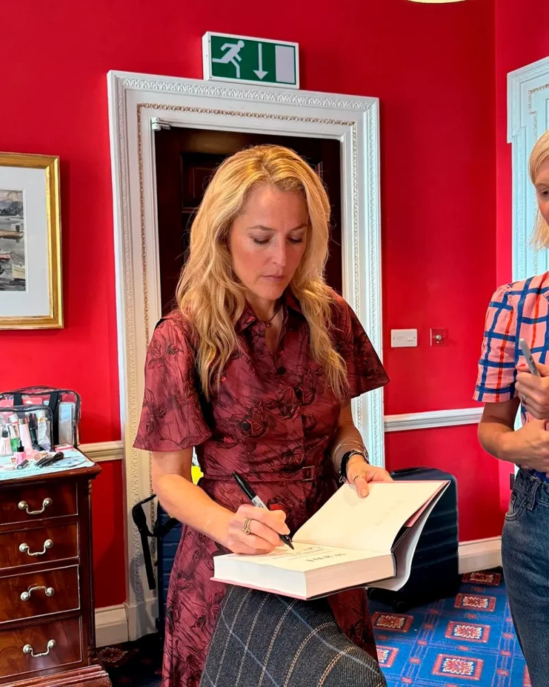 Gillian Anderson firmando una dedicatoria sobre una copia de uno de sus libros