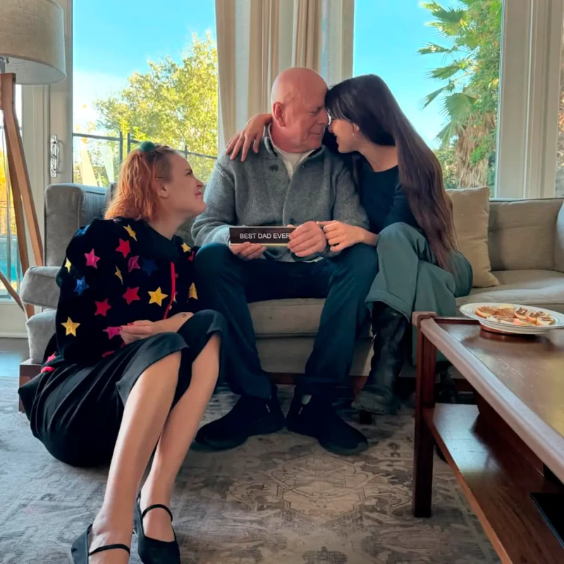 Bruce willis acompañado por sus hijas en el salón de su casa.