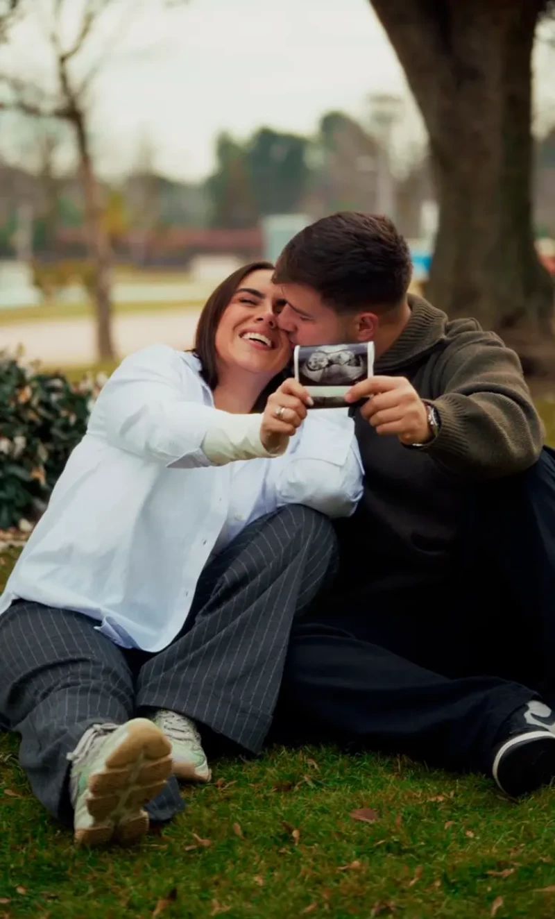 Sol Macaluso con su novio sentados en un parque enseñando la ecografía de su embarazo.