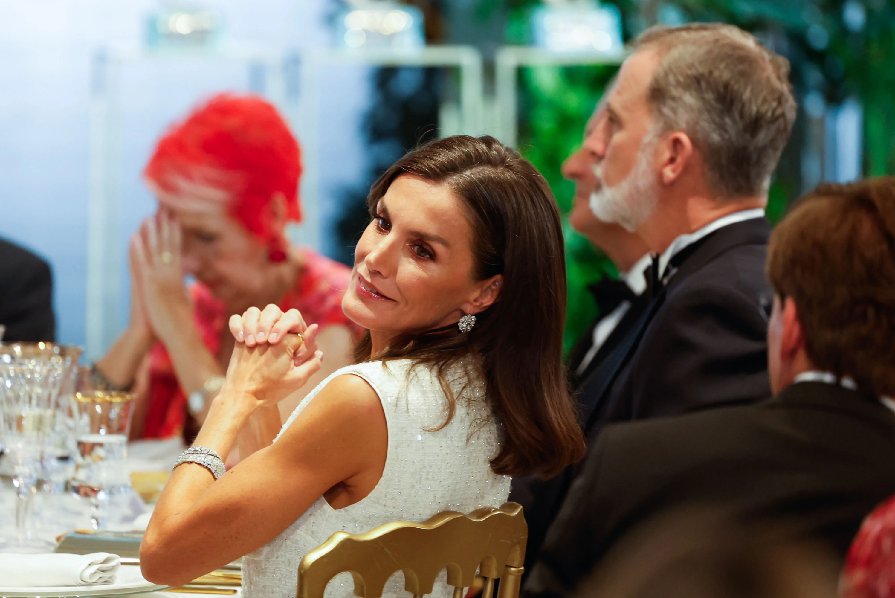 La reina Letizia sentada, de blanco y con joyas.