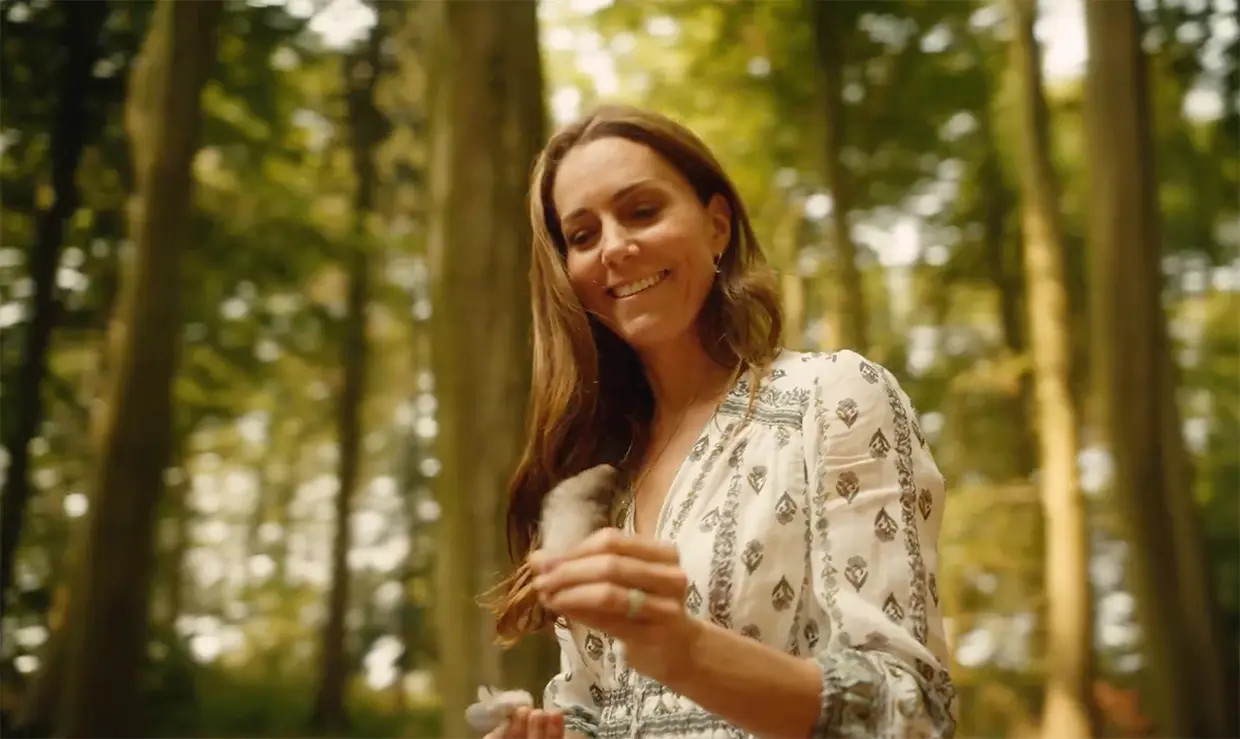 Kate Middleton sonriente con una pluma de ave en su mano dentro de un bosque